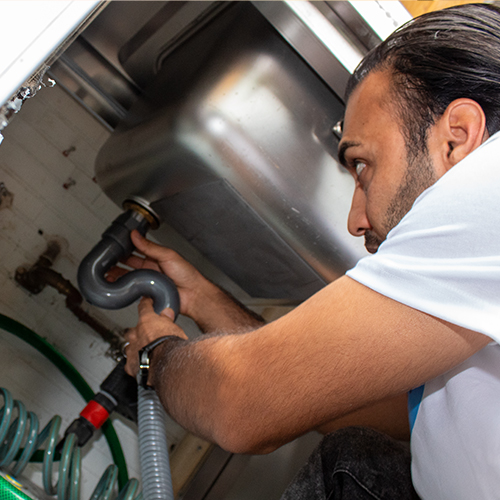 Ein Mitarbeiter von Sauber In Form repariert ein Rohr unter einem Spülbecken in einer Küche.