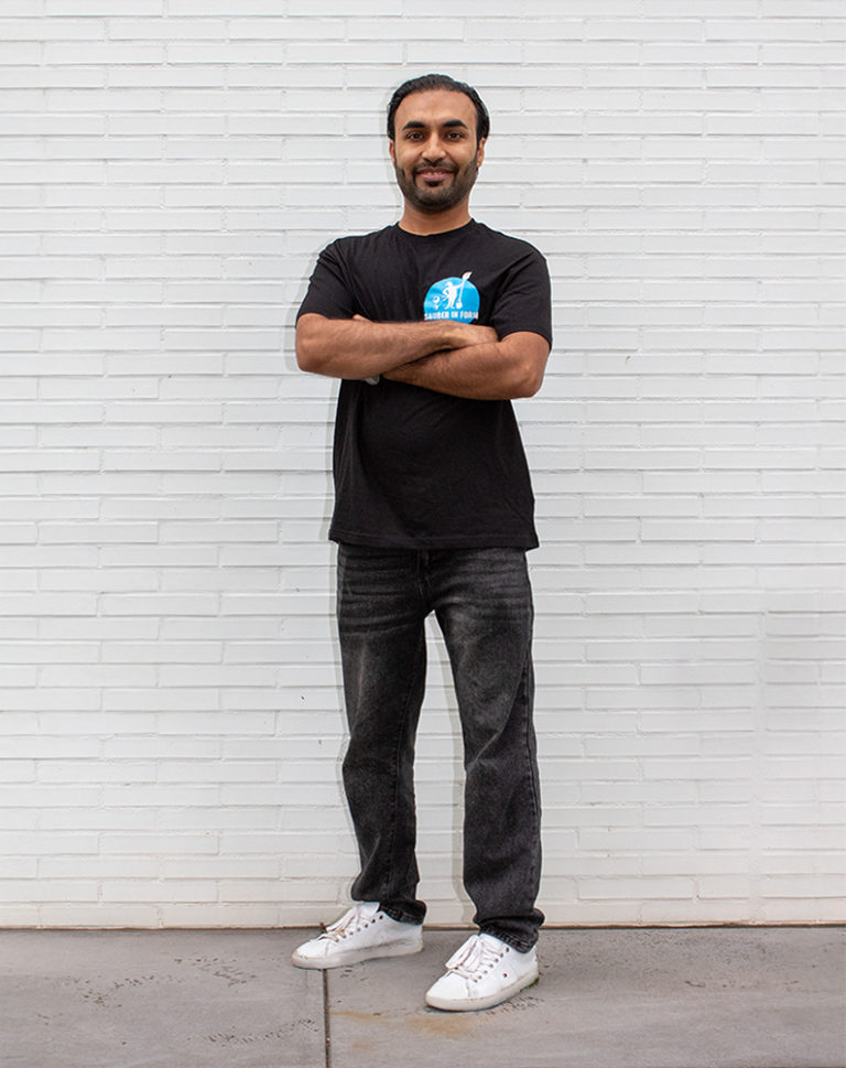 Ein Mitarbeiter von Sauber In Form steht lächelnd mit verschränkten Armen vor einer weißen Wand.