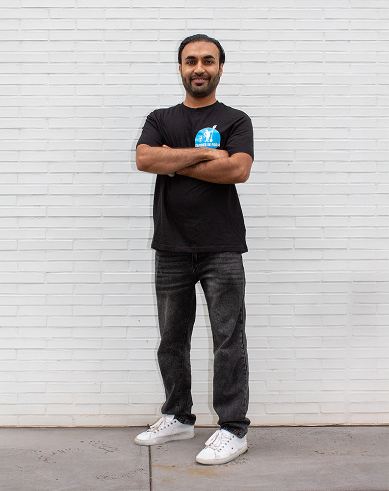 Ein Mitarbeiter von Sauber In Form steht lächelnd mit verschränkten Armen vor einer weißen Wand.