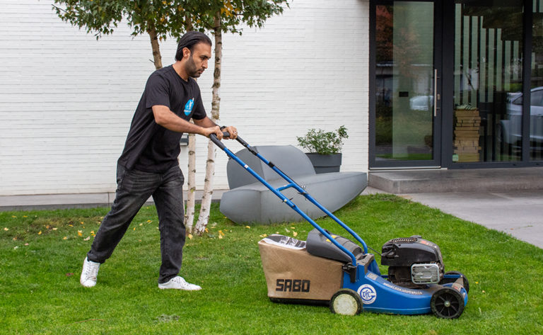 Ein Mitarbeiter von Sauber In Form mäht den Rasen vor einem modernen Gebäude mit einem Rasenmäher.