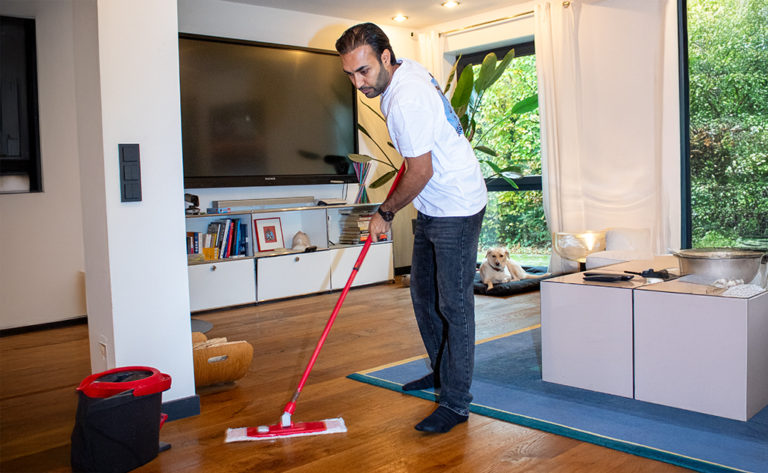 Ein Mitarbeiter von Sauber In Form führt eine gründliche Bodenreinigung in einem modernen Wohnzimmer durch.