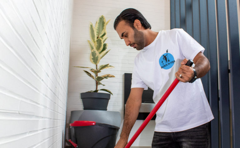 Ein Reinigungskraft von Sauber In Form wischt sorgfältig den Boden im Treppenhaus eines Wohngebäudes.