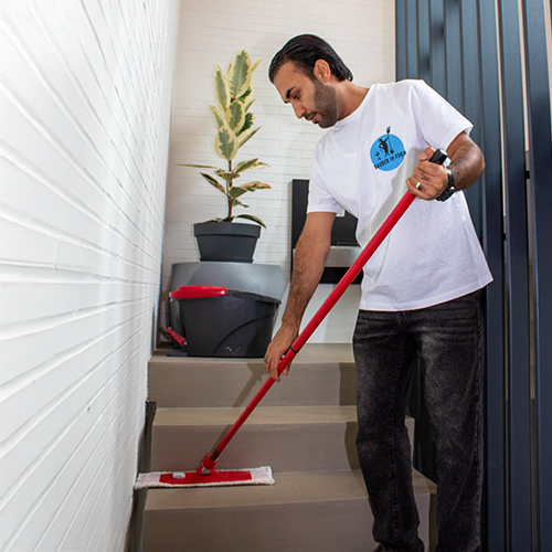 Ein Mitarbeiter von Sauber In Form wischt sorgfältig den Boden im Treppenhaus eines gepflegten Gebäudes.