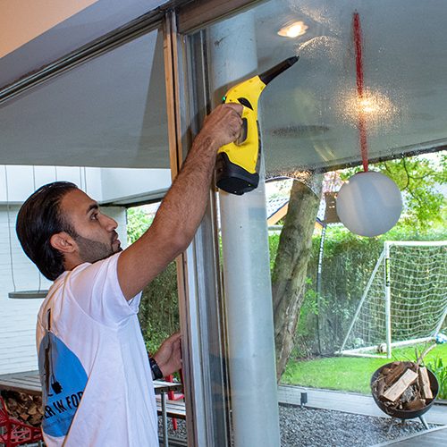 Ein Mitarbeiter von Sauber In Form reinigt die Fensterscheiben eines Gebäudes mit einem Dampfreiniger.