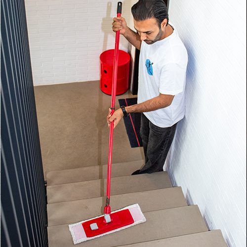 Ein Mitarbeiter von Sauber In Form reinigt sorgfältig die Treppen mit einem roten Wischmopp.